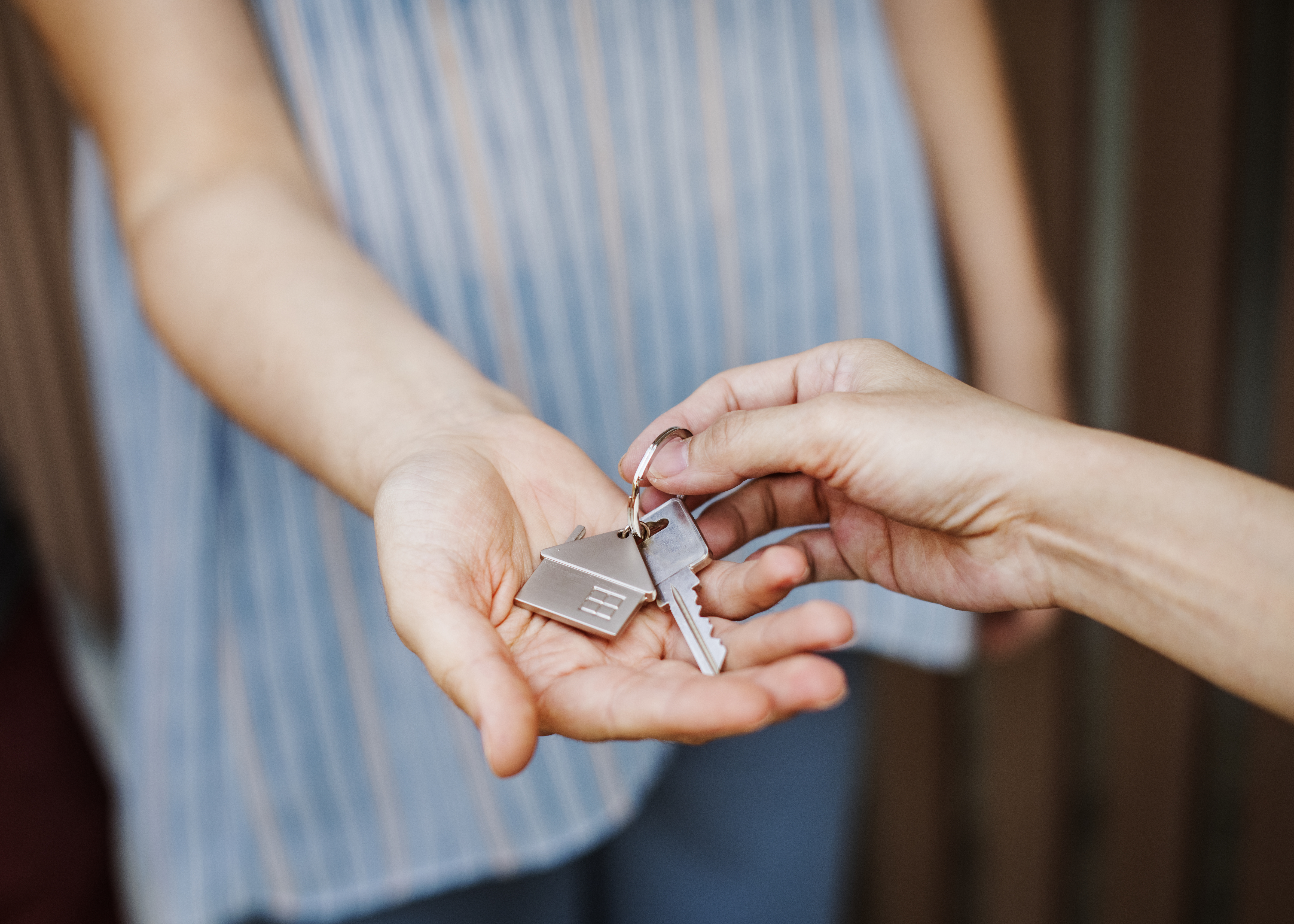 Keys with a key ring in the shape of a house, is being exchanged between two people.