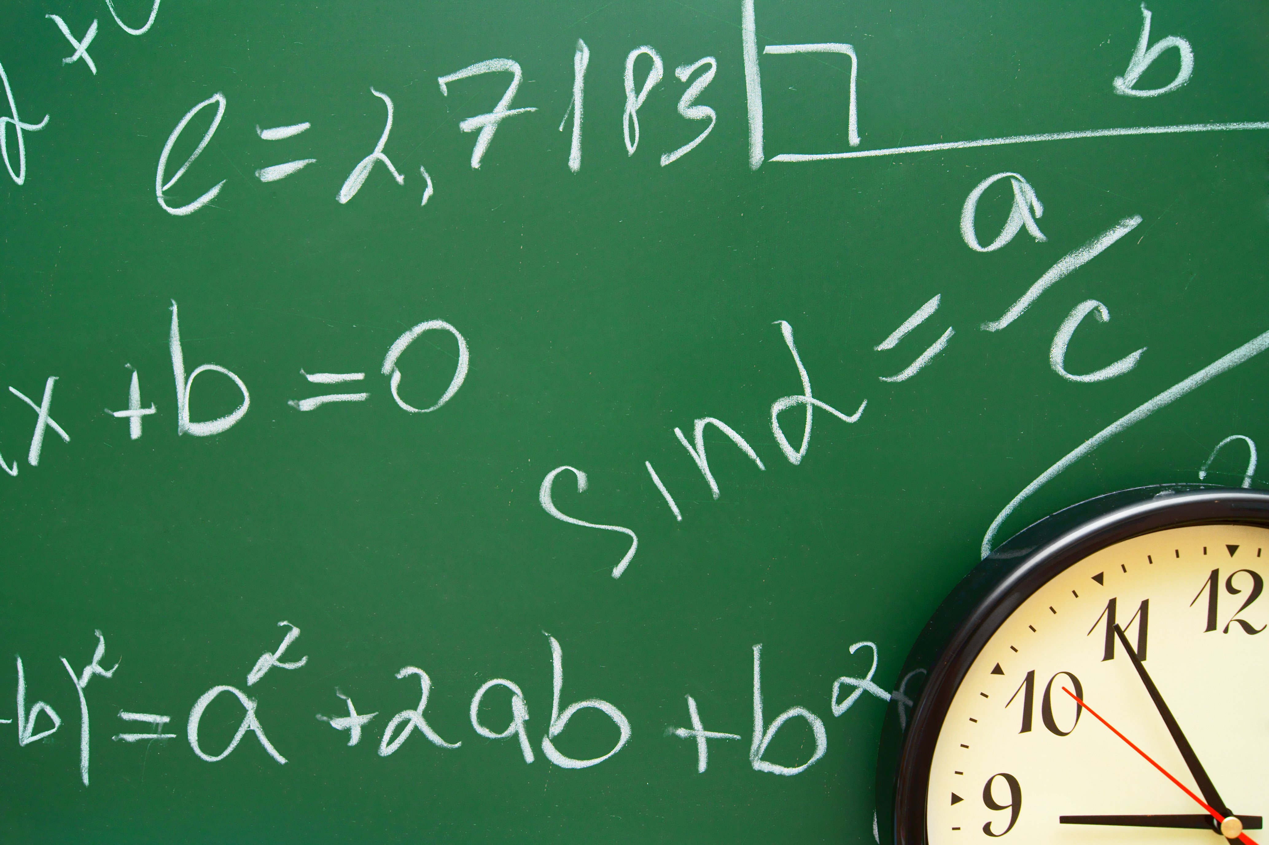 A classroom chalkboard displaying various mathematical expressions in white chalk, including trigonometric and algebraic equations. A clock showing 10:10 is partially visible in the bottom corner.