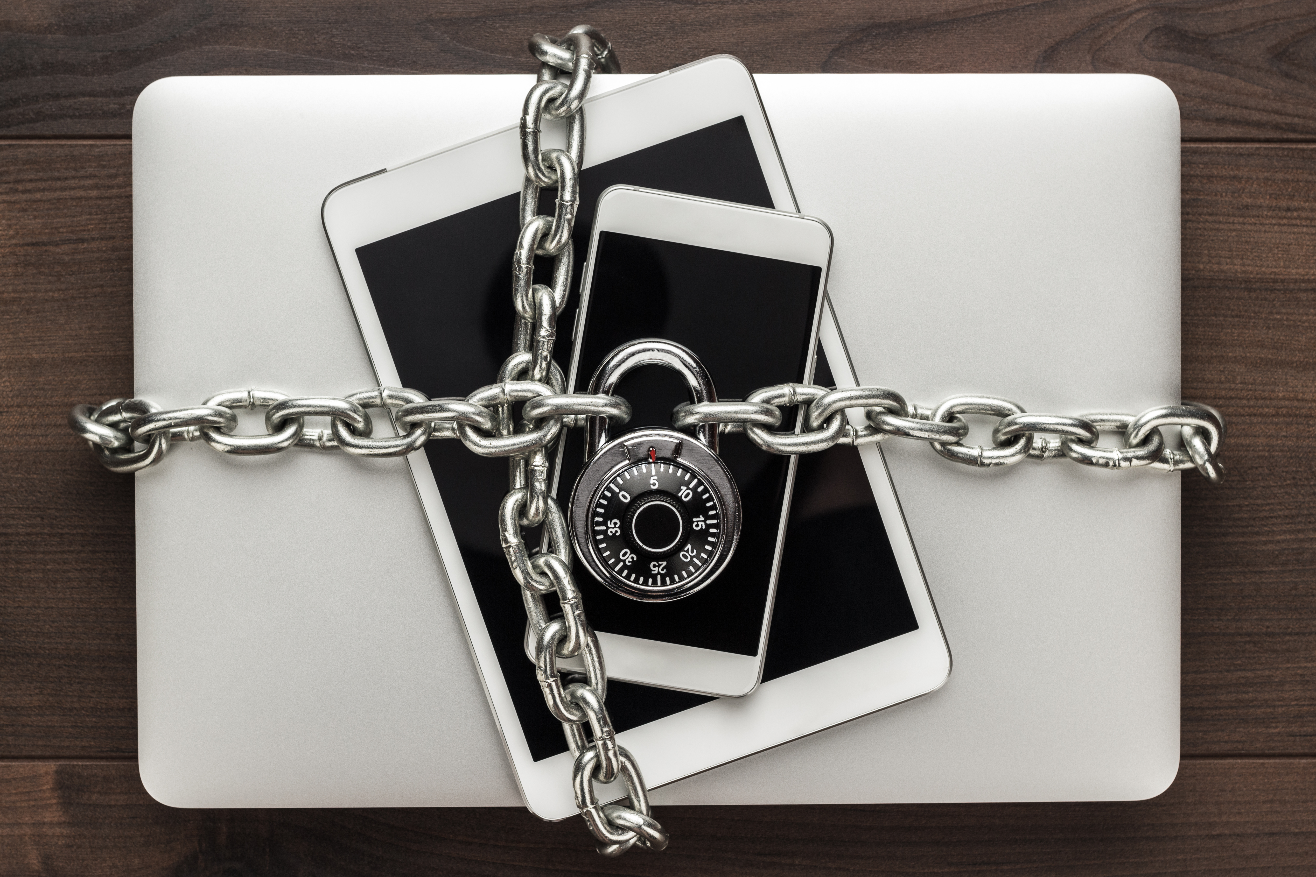 Electronic devices including a laptop, tablet, and smartphone bound by a metal chain with a padlock, representing data privacy and cybersecurity.